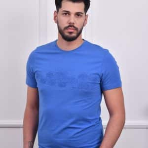 Muškarac nosi plavu majicu sa diskretnim printom na prednjem delu, u jednostavnom stilu sa kratkim rukavima, idealnu za casual prilike.